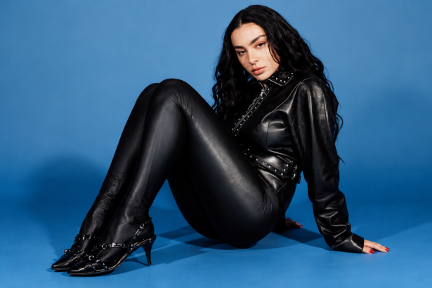 Charli XCX press photo in black leather against a blue backdrop, 'Music, Fashion, Film' Tour era.