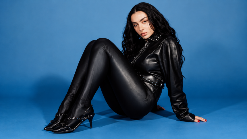 Charli XCX press photo in black leather against a blue backdrop, 'Music, Fashion, Film' Tour era.